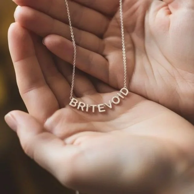 A silver BRITEVOID necklace held in a hand